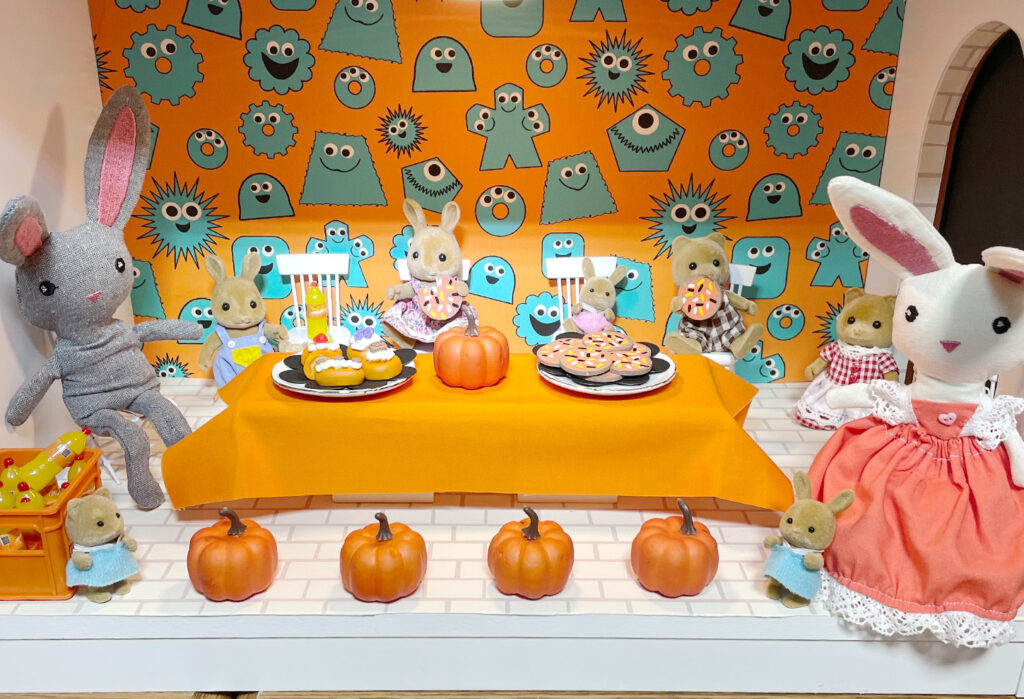 Bunnies and bears sitting around a table heaped with cakes, cookies, and pumpkins. 